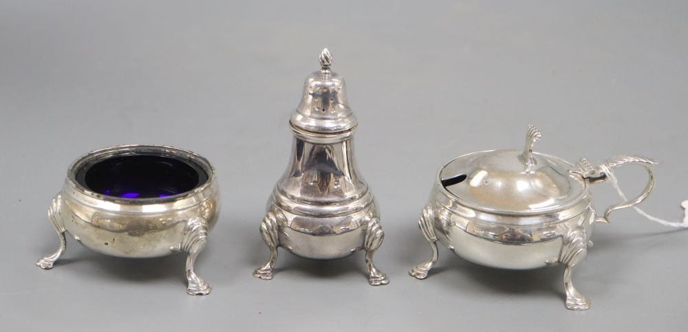 A silver three piece cruet set, with embossed girdle, three paw feet and blue glass liner, comprising a mustard pot, a salt and a peppe